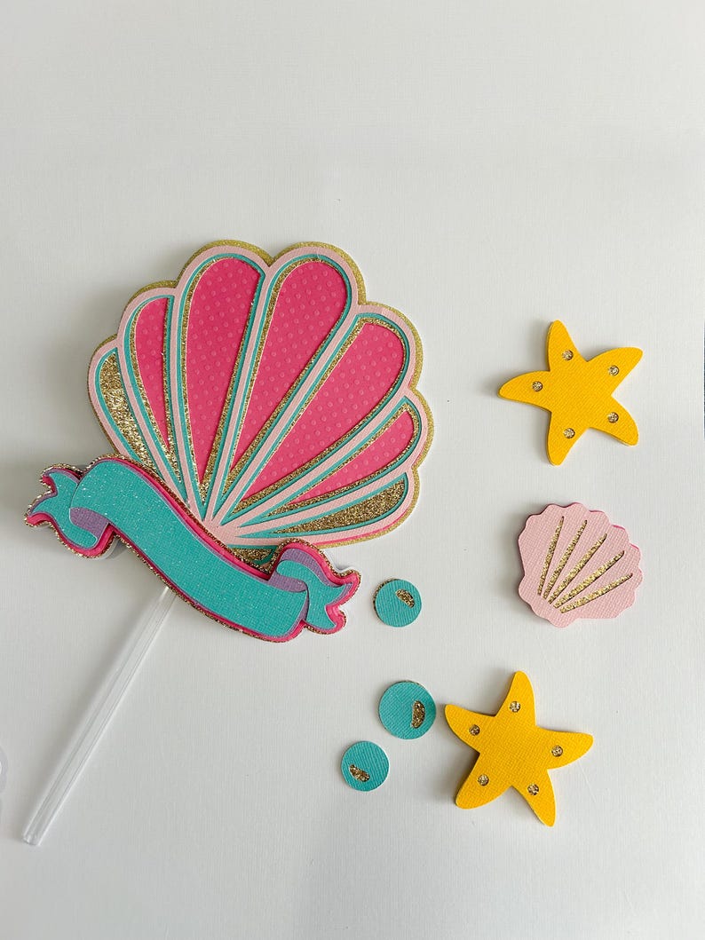 May include: A pink and gold glitter seashell with a turquoise ribbon, two yellow starfish, and a pink seashell with gold glitter accents.