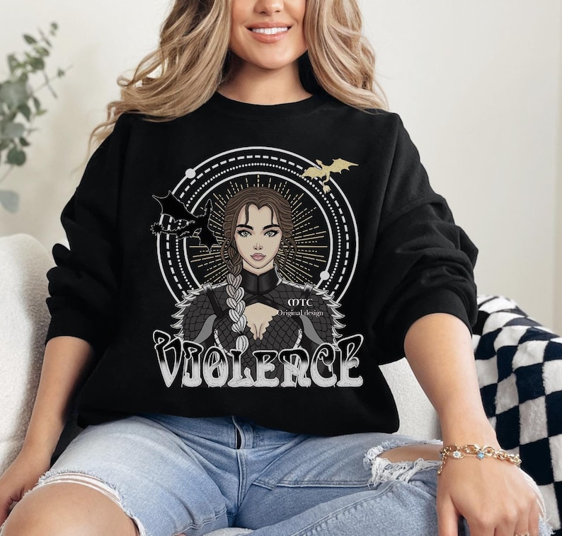 May include: Black sweatshirt featuring a graphic design of a woman with long blonde hair, wearing a black leather jacket with a dragon design. The text "VIOLERCE" is printed in white below the graphic. The text "OTC Original Design" is printed in white in the bottom right corner of the graphic.