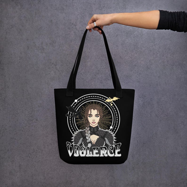 May include: Black tote bag featuring a white graphic of a woman with long brown hair wearing a black and silver outfit. The graphic is surrounded by a circle with a black dragon and the word "VIOLENCE" in white letters.