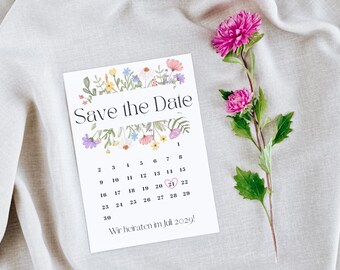 May include: A white card with the text "Save the Date" and a calendar layout, adorned with floral illustrations. A pink flower with green leaves is placed next to the card. The text "Wir heiraten im Juli 2029!" is at the bottom.