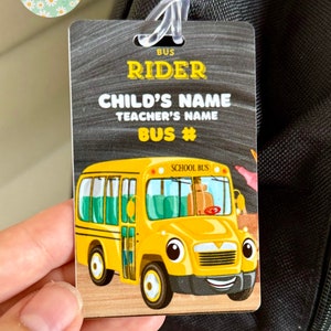 Pu&ograve; includere: Un autobus scolastico giallo con un viso sorridente e le parole "School Bus" sul lato. L'autobus &egrave; su uno sfondo di lavagna nera con il testo "Bus Rider", "Nome del bambino", "Nome dell'insegnante" e "Numero di autobus".