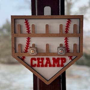 May include: Wooden baseball-themed ring holder with red stitching and the word "CHAMP" in red letters. Two rings are displayed in the holder.