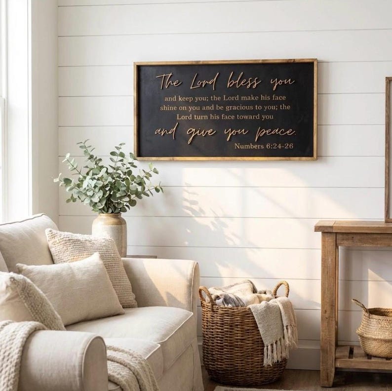 May include: A rectangular wall sign with a black background and a natural wood frame. The sign features raised, light-colored lettering that reads: The Lord bless you and keep you; the Lord make his face shine on you and be gracious to you; the Lord turn his face toward you and give you peace Numbers 6:24-26.
