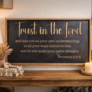 May include: A rectangular wooden sign with a black background and a natural wood frame. The sign features gold-colored lettering that reads: Trust in the Lord and lean not on your own understanding; in all your ways submit to him, and he will make your paths straight. Proverbs 3:5-6.