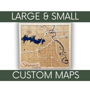 May include: A wooden map of Shreveport, Louisiana, with a blue lake and a winding river. The map is framed and has the text "Shreveport, Louisiana" and "CUSTOM MAPS" below it. The text "LARGE & SMALL" is at the top of the image.