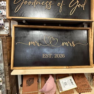 May include: Two rectangular wooden signs with black backgrounds and light wood frames. The top sign features the text "All my life you have been faithful with every breath that I am able oh, I will sing of the Goodness of God". The bottom sign displays "mr" and "mrs" with two connected hearts and "EST. 2026".