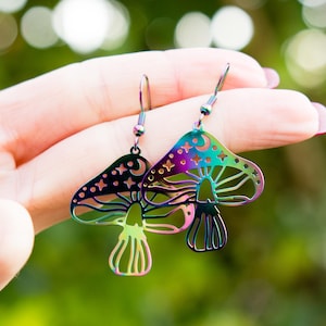 Könnte beinhalten: Ein Paar regenbogenfarbene, schimmernde Pilz-Ohrringe mit einem Halbmond- und Sternen-Design. Die Ohrringe sind aus Edelstahl und haben ein baumelndes Design.
