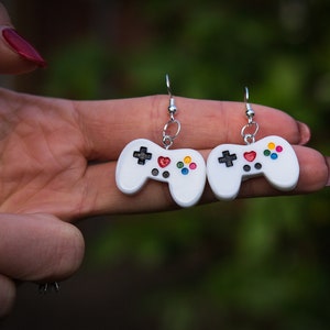 Könnte beinhalten: Ein Paar weiße Videospiel-Controller-Ohrringe mit bunten Knöpfen und einem roten Herzen auf jedem Controller.