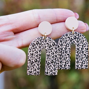 May include: A pair of cream-colored arch-shaped earrings with a black and cream leopard print design.