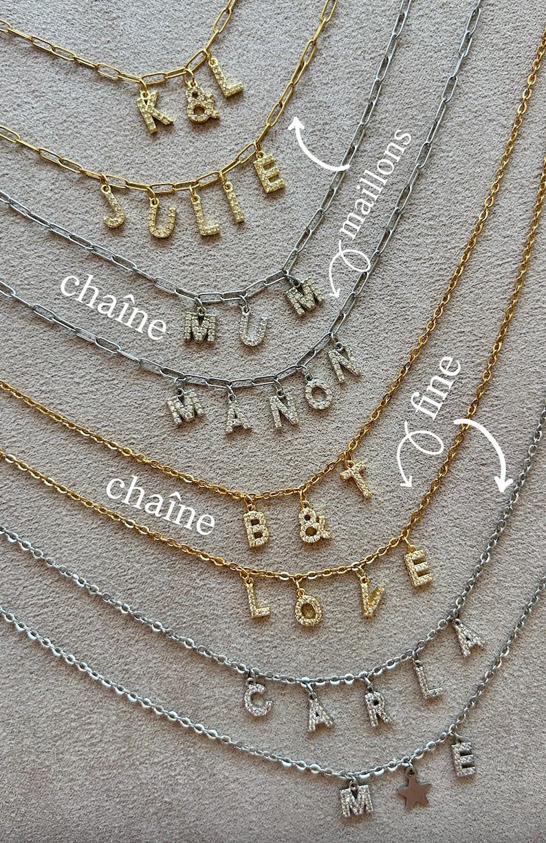 May include: A collection of gold and silver chain necklaces with pendant letters spelling out names. The letters are encrusted with small, sparkling stones. The necklaces are displayed on a neutral-toned surface.