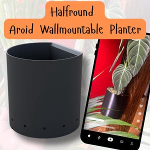 Może przedstawiać: Czarny, półokrągły, montowany na ścianie pojemnik na rośliny. Pojemnik ma otwory drenażowe i jest pokazany zamontowany na ścianie z rośliną w środku.