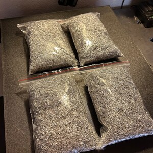 May include: Four clear plastic bags filled with silver metal shavings. The bags are on a black surface.