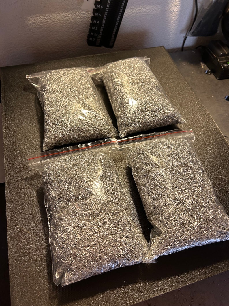 May include: Four clear plastic bags filled with silver metal shavings. The bags are on a black surface.