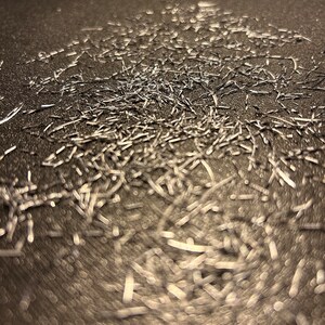 May include: A close-up image of a metallic surface covered in a large amount of silver glitter. The glitter is scattered randomly across the surface, creating a shimmering effect.