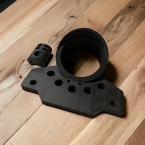 May include: Black plastic parts for a 3D printed model. The parts include a round cylinder with a hole in the center and a flat piece with multiple holes.
