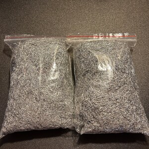 May include: Two clear plastic bags filled with silver metallic shredded packing material.