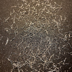 May include: A close-up of a dark brown surface with a pattern of thin, white lines. The lines are randomly arranged and create a textured effect.
