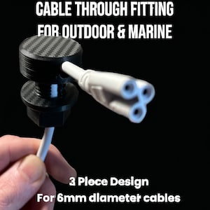 Puede incluir: Un accesorio negro para pasar cables con un patrón de fibra de carbono. El accesorio está diseñado para uso en exteriores y en ambientes marinos. Es un diseño de 3 piezas para cables de 6 mm de diámetro.