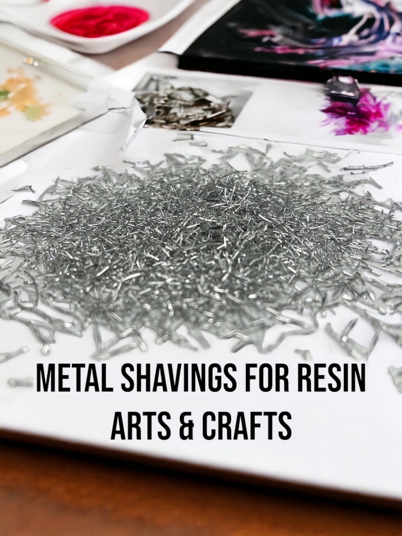 May include: A white plate filled with silver metal shavings. The plate is on a wooden surface. The text "METAL SHAVINGS FOR RESIN ARTS & CRAFTS" is printed below the plate.