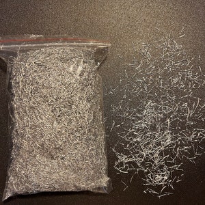 May include: A clear plastic bag filled with silver metallic strands. Some strands are scattered on a dark surface.