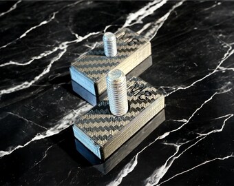 May include: Two black carbon fiber blocks with silver metal screws. Each block has the text "M12" printed on it.