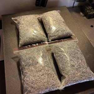 May include: Four clear plastic bags filled with silver metal shavings. The bags are arranged in two rows of two on a black surface.