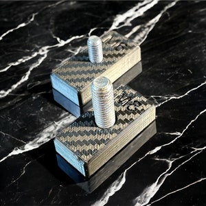 May include: Two black carbon fiber blocks with silver metal screws. Each block has the text "M12" printed on it.