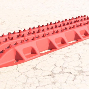 May include: A red traction mat with a ridged surface and numerous conical spikes. The mat is designed to provide grip for vehicles stuck in sand, mud, or snow. The mat is approximately 40 inches long.