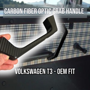May include: A black carbon fiber optic grab handle for a Volkswagen T3. The handle is made of a durable material and has a sleek, modern design.