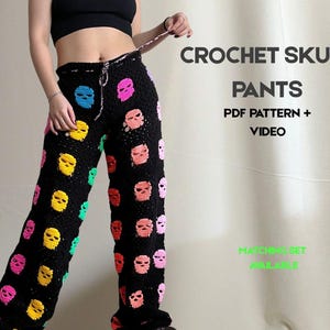 May include: Black crochet pants adorned with colorful skull motifs. The pants feature a drawstring waist and are decorated with skulls in shades of pink, yellow, blue, and green. Text on the image reads "CROCHET SKULL PANTS PDF PATTERN + VIDEO".