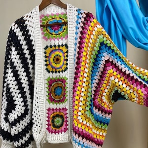 Può includere: Un cardigan bianco in crochet con un pannello a righe bianco e nero sul lato sinistro e un pannello arcobaleno colorato sul lato destro. Il cardigan ha una vestibilità ampia e maniche lunghe.