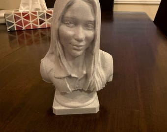 May include: A white plaster bust of a person with long hair. The bust is on a wooden table.