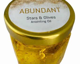 May include: A small glass jar with a gold lid and a white label that reads "ABUNDANT Stars & Olives Anointing Oil". The jar is filled with a clear, yellow liquid with gold flakes.
