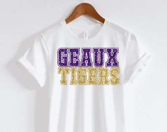 May include: White t-shirt with the words "GEAUX TIGERS" in purple and gold glitter.