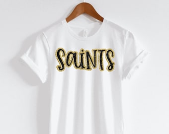 May include: White t-shirt with black glitter lettering that says "Saints".