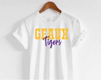 May include: White t-shirt with the text "GEAUX Tigers" in gold and purple lettering.