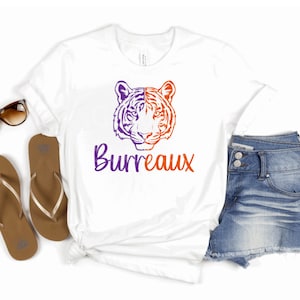 May include: White t-shirt with a purple and orange tiger head graphic and the text "Burreaux" in purple.