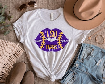 May include: A white t-shirt with a purple lips design. The lips are outlined in yellow and have the words "LSU Tigers." printed inside.