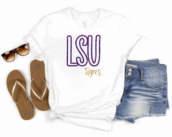 Może przedstawiać: Biała koszulka z purpurowym, błyszczącym logo LSU i złotym, błyszczącym napisem "Tigers".