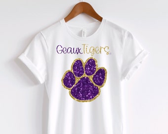 May include: White t-shirt with the text "Geaux Tigers" and a purple and gold glitter paw print.
