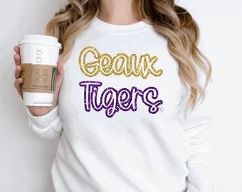 May include: White sweatshirt with gold glitter "Geaux" and purple glitter "Tigers" text.