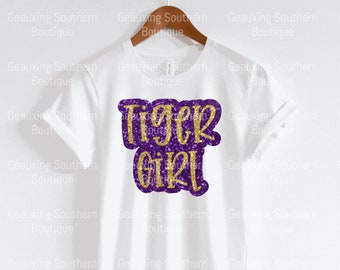 May include: White t-shirt with a purple and gold glitter design that says "Tiger Girl".