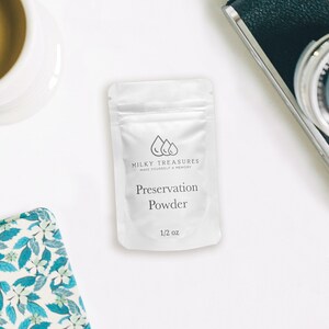 Może przedstawiać: Biały woreczek z srebrnym zamkiem błyskawicznym, zawierający biały proszek. Woreczek ma nadrukowany tekst "MILKY TREASURES MAKE YOURSELF A MEMORY" i "Preservation Powder 1/2 oz".