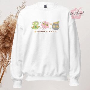 May include: White sweatshirt with a green leprechaun hat, a shamrock, a pot of gold, and the text "GROOVING!" printed on the front.