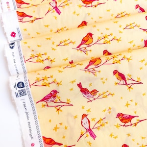 May include: Yellow fabric with a repeating pattern of pink and orange birds on branches with yellow stars. The fabric has a white border with text that reads "#WeareFabrics #MCEMargold".