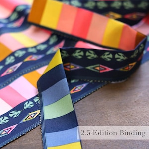 May include: Colorful ribbon with striped and patterned designs. The ribbon features a variety of colors, including yellow, orange, pink, and blue. The text "2.5 Edition Binding" is visible on the ribbon.