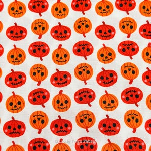 May include: A white fabric featuring a repeating pattern of orange jack-o'-lanterns with black eyes, noses, and jagged mouths. The pumpkins are arranged in a grid, each displaying a distinct facial expression with small pink cheek accents.