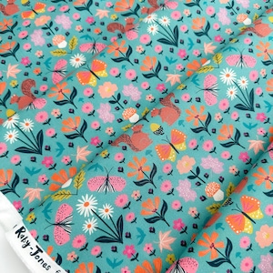 May include: Teal fabric with a repeating pattern of pink, orange, and yellow flowers, butterflies, and squirrels. The fabric has a white border with the text "Roxy-Jones for dashwood" printed on it.