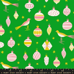 May include: A green fabric featuring a repeating pattern of pink and white Christmas ornaments, yellow birds, and small yellow stars. A black ruler at the bottom shows measurements in inches, with the text Ruby Star Society printed repeatedly.
