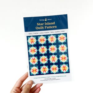 May include: A clear plastic package containing a "Star Island Quilt Pattern" by String & Story. The pattern features a geometric design with star shapes in orange, yellow, and teal on a navy blue background. The package includes sizes for small throw, large throw, twin, queen, and king quilts.